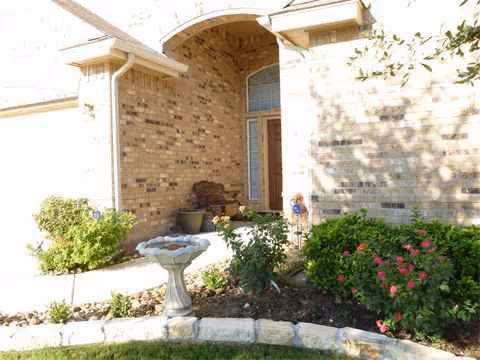 The brick building entrance features an arched doorway and a small landscaped garden with a birdbath.