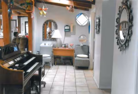 Indoor senior living lounge with a piano, seating, desk, mirrors, and warm lighting.