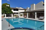 Outdoor swimming pool area at a senior living facility with lounge chairs and a two-story building in the background under a clear sky.