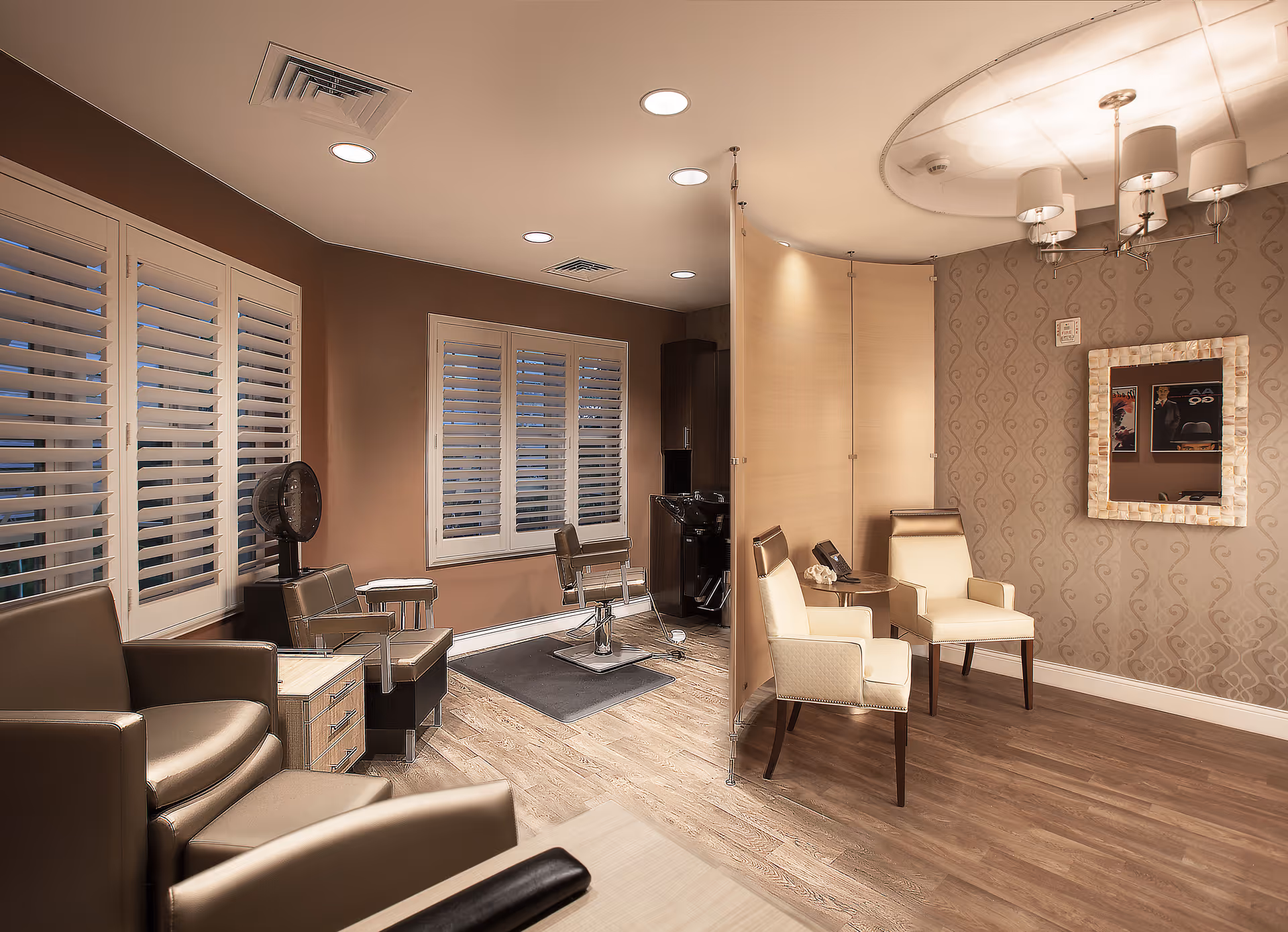 Interior view of a stylish salon area with multiple chairs, a hair washing station, a partition, and a decorative wall with a mirror and chandelier lighting.