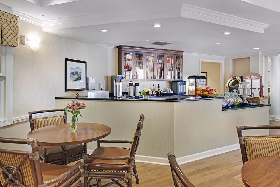 Bright communal dining area with round wooden tables and chairs in front of a coffee and snack counter.