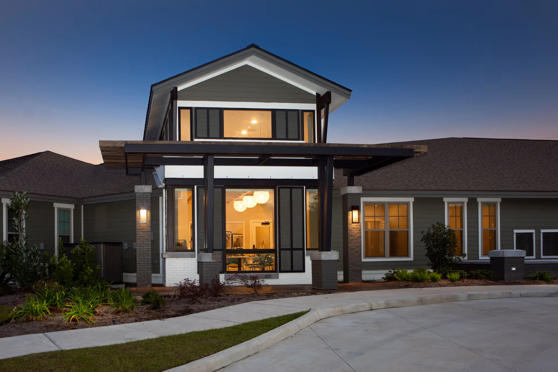 Front exterior of a modern two-story senior living building at dusk with illuminated windows and a covered entrance.