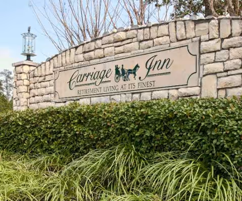 Stone entrance sign for Carriage Inn retirement living, set in a stone wall with greenery.