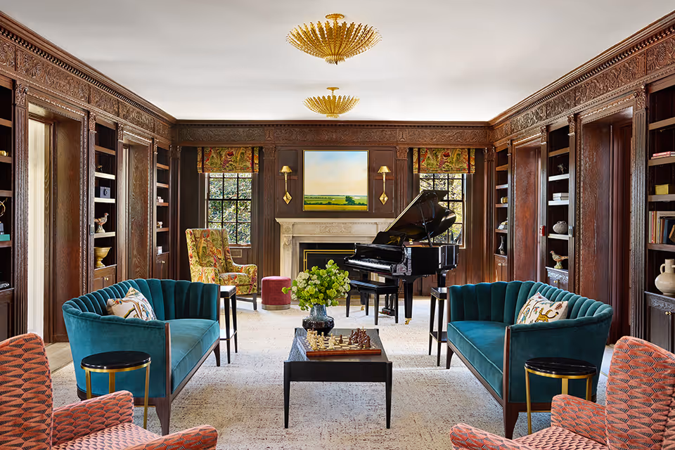 Elegant wood-paneled living room with teal sofas facing a coffee table and a grand piano by a fireplace.