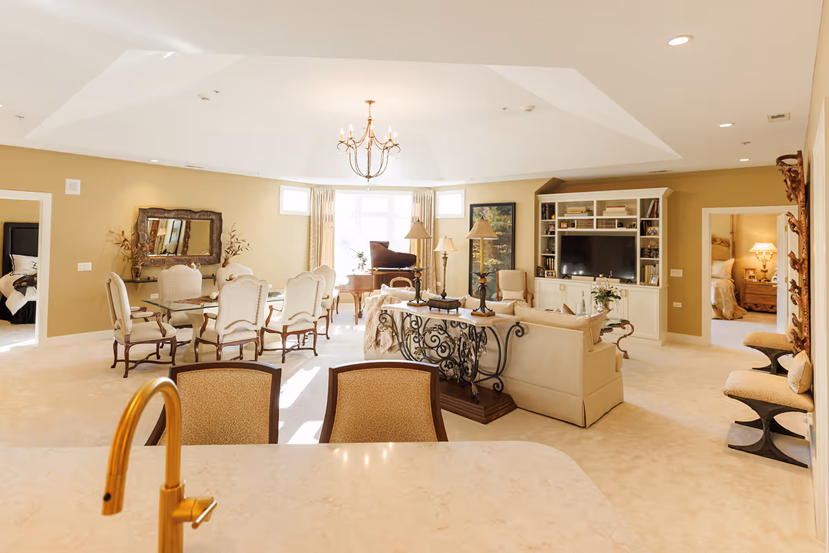 Bright, open living and dining area with cream furnishings, a sofa and chairs, dining table, chandelier, piano, and built-in entertainment center.