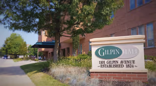 Brick exterior of Gilpin Hall showing the entrance, landscaping, sidewalk, and a stone sign reading 'Gilpin Hall 1101 Gilpin Avenue — Established 1824'.