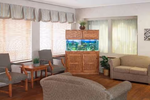 Cozy senior living lounge with seating, an aquarium, and large windows.