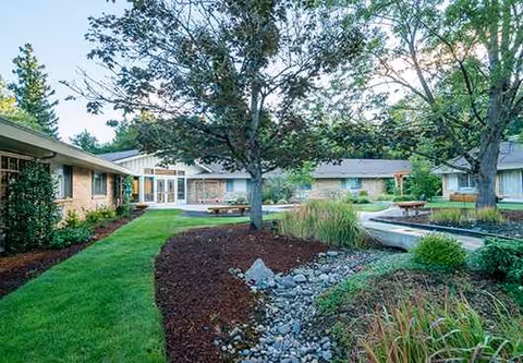 Exterior view of a senior living courtyard with trees, walkways, and landscaped garden beds.