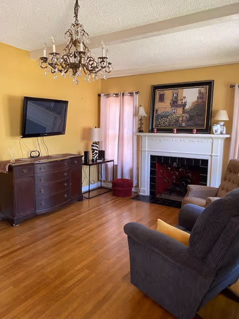 A cozy living room with a chandelier, television, and vintage furniture.