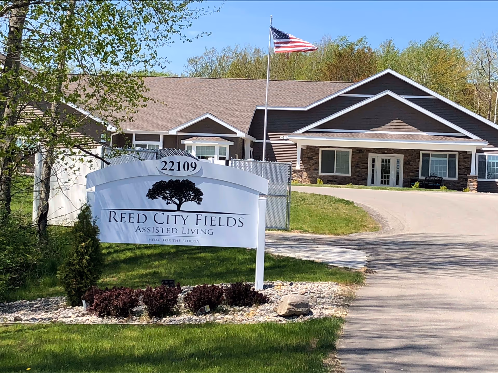 Sign and front entrance of Reed City Fields assisted living facility with an American flag flying above.