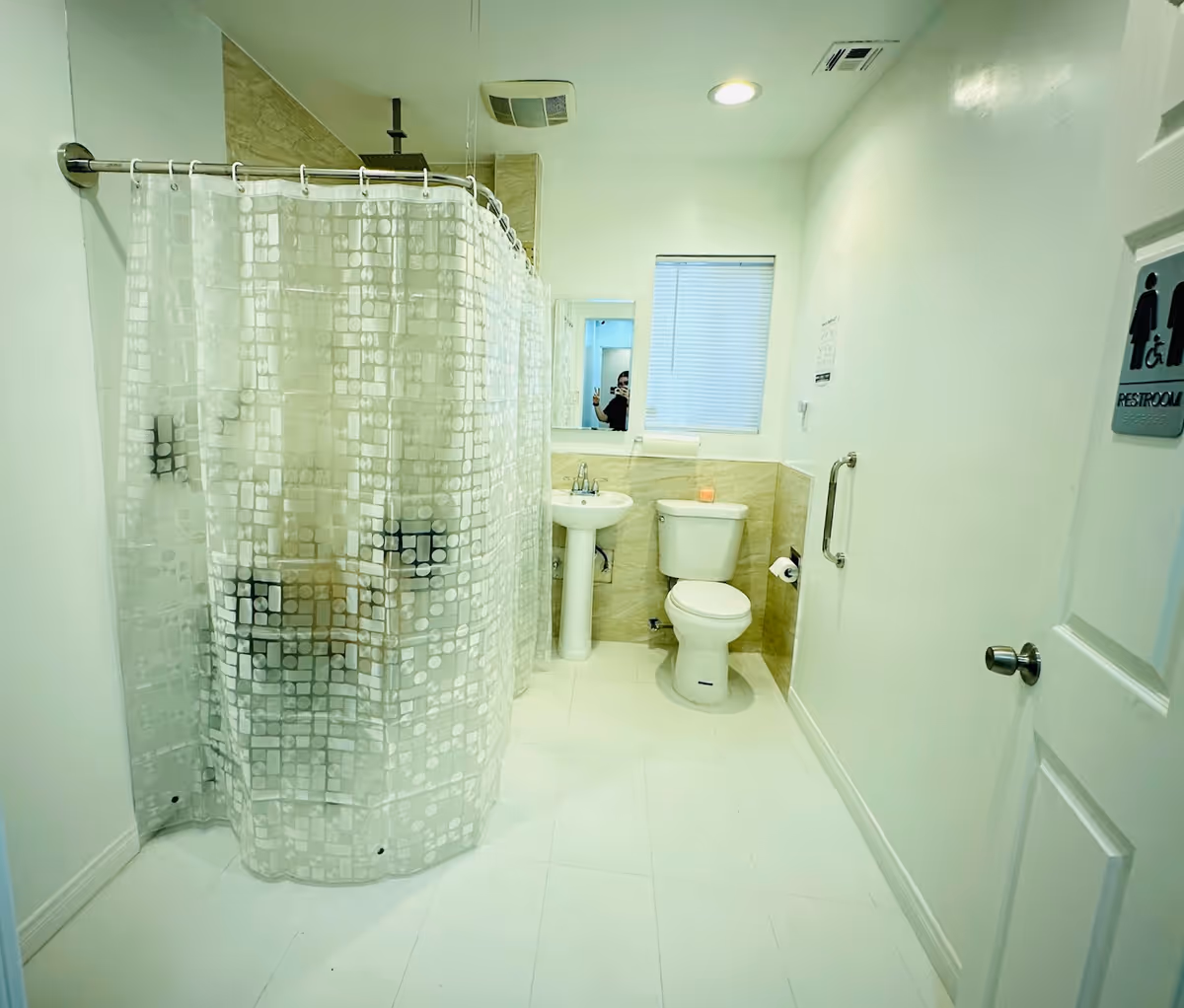 Accessible bathroom with shower curtain, sink, toilet, and restroom sign.