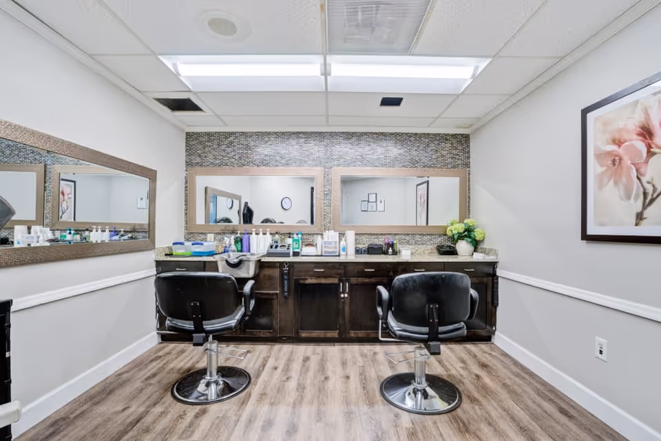 Interior salon area with two black styling chairs facing a mirrored countertop stocked with hair products.