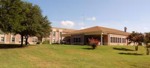 Single-story senior living facility with a covered entrance, lawn, and trees.