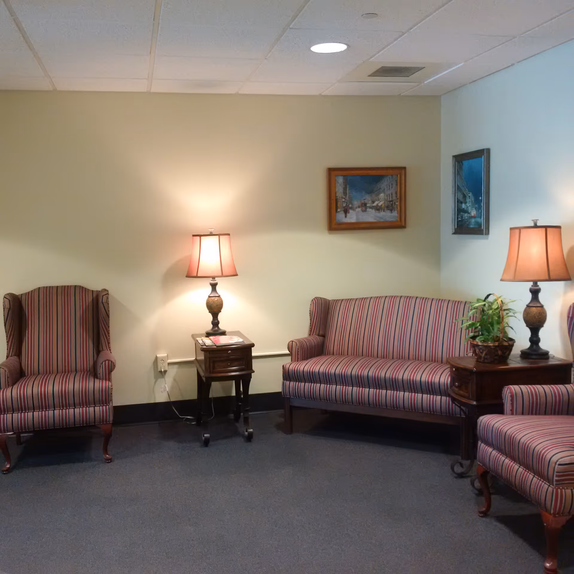 Seating area with striped armchairs and a matching sofa, side tables with lamps and framed pictures on the wall.