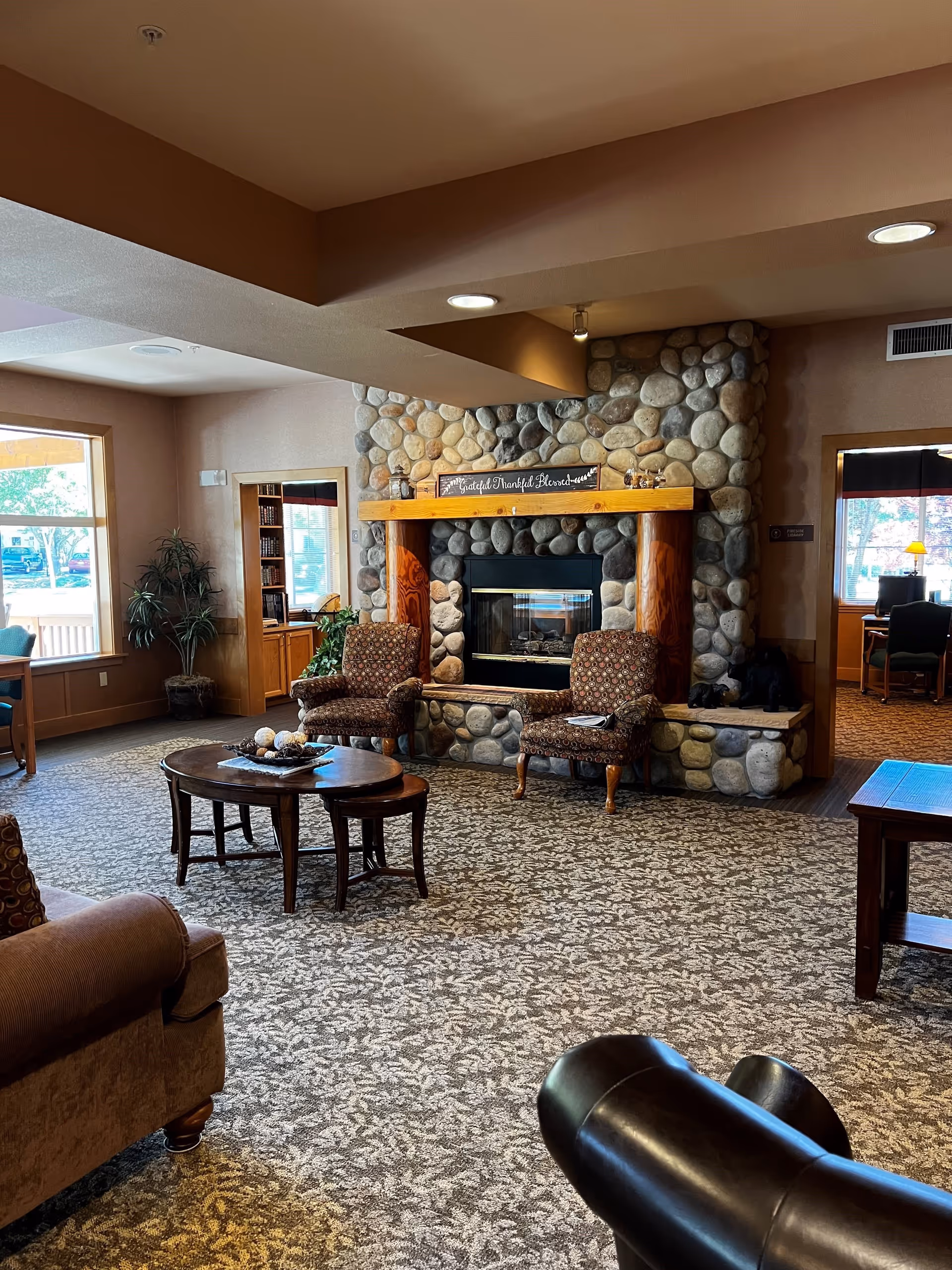 Cozy common lounge with a stone fireplace flanked by armchairs, coffee tables, and large windows.