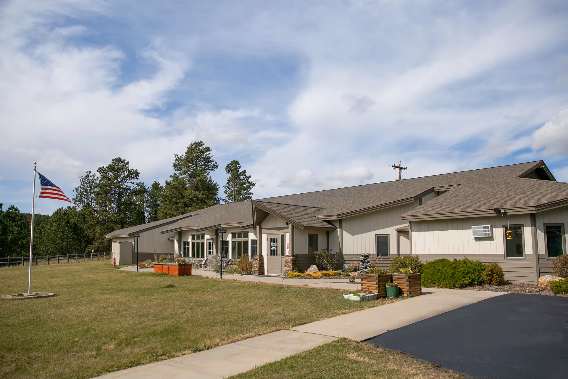 Single-story assisted living building with a front lawn and an American flag under a partly cloudy sky.