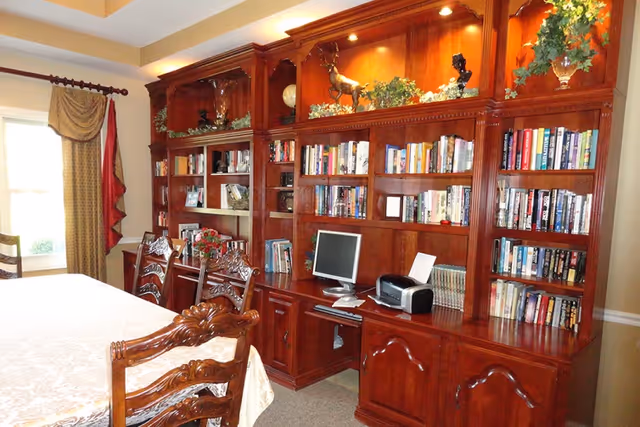Dining room with an ornate wooden table and chairs and a large built-in wooden bookshelf/office unit filled with books, a computer, and decorative items.