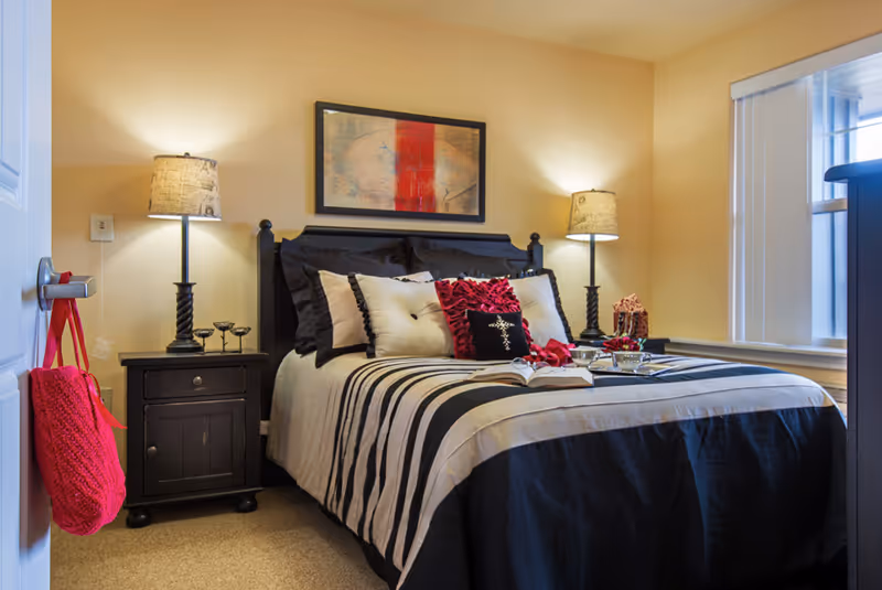 Neatly made bed with black-and-white striped bedding and decorative pillows, flanked by two bedside tables with lamps, artwork above the headboard, and a window to the right.