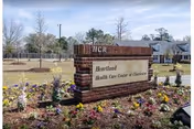 Exterior brick sign at a senior care facility with a flower bed.