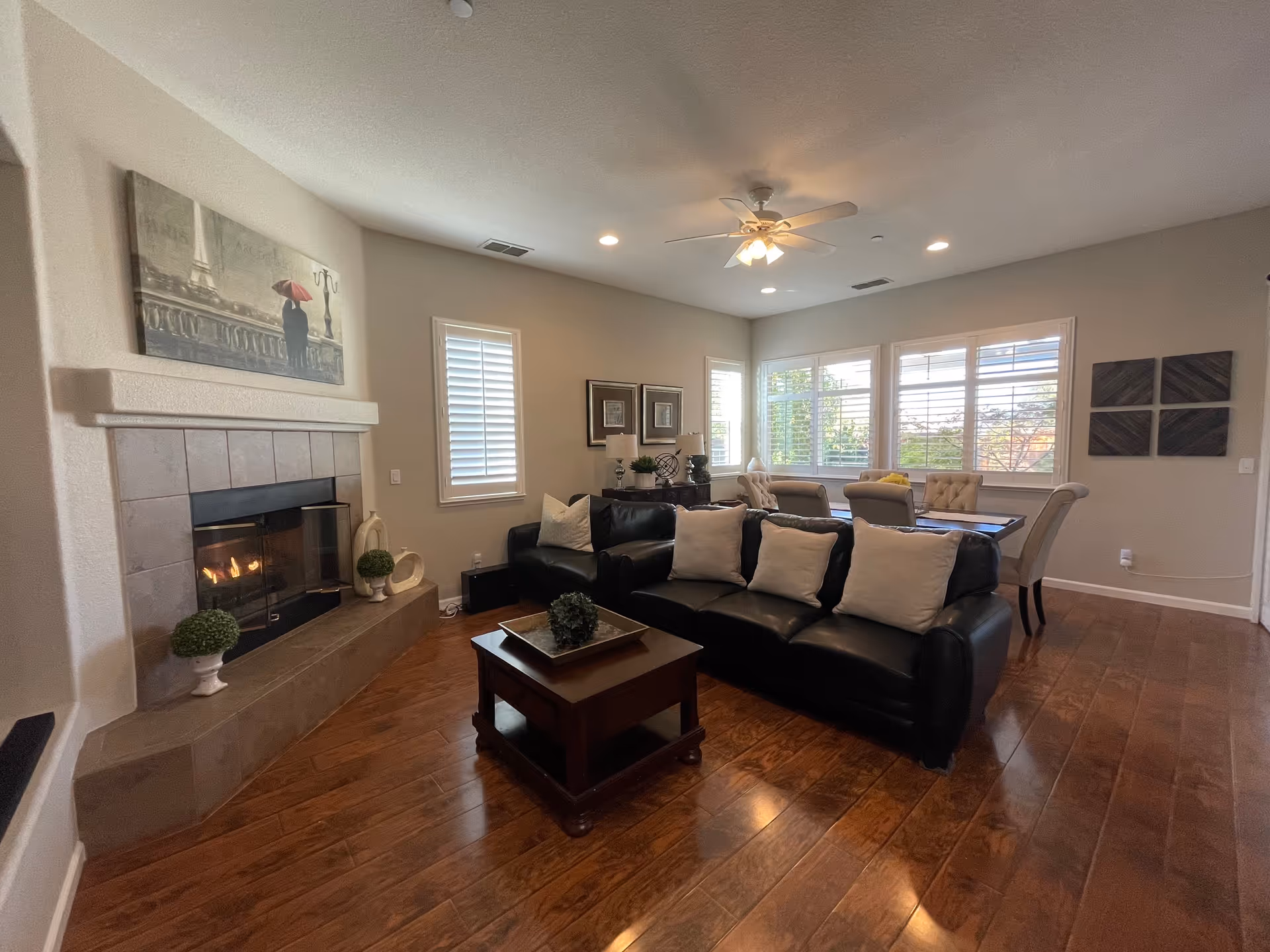 Spacious living room with a black leather sofa, coffee table, fireplace, and a dining area by large windows.