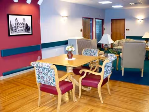 Colorful senior living dining room with wooden table, upholstered chairs, flowers, and lamps.