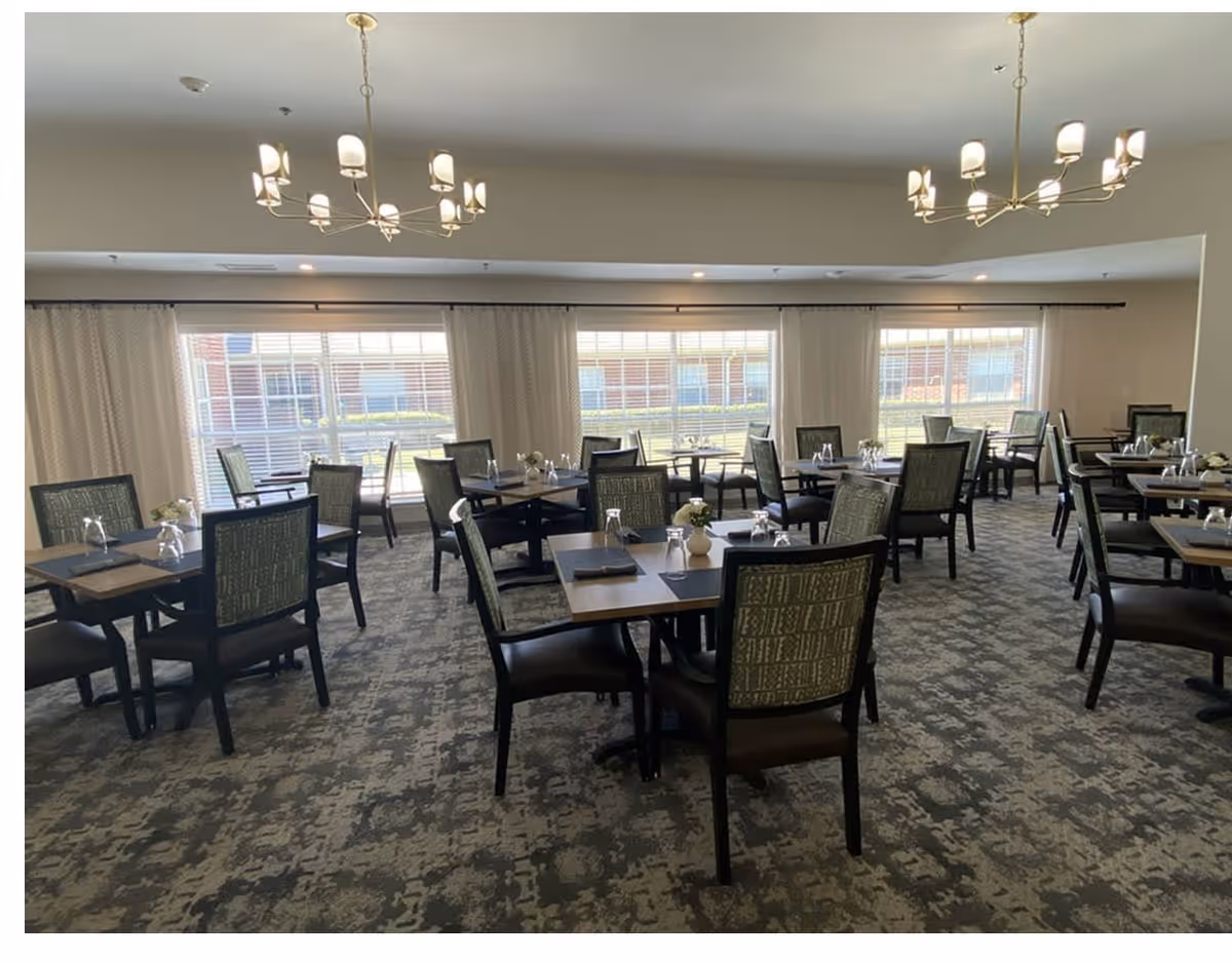 Spacious dining room with multiple set tables and chairs, chandeliers, and large windows.