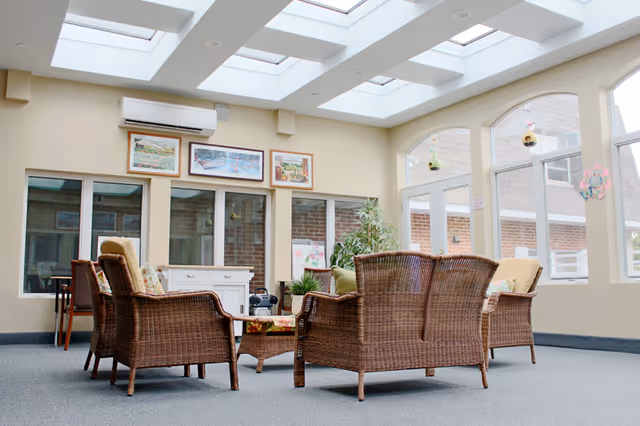Bright common sitting area with wicker chairs arranged around a coffee table under skylights.