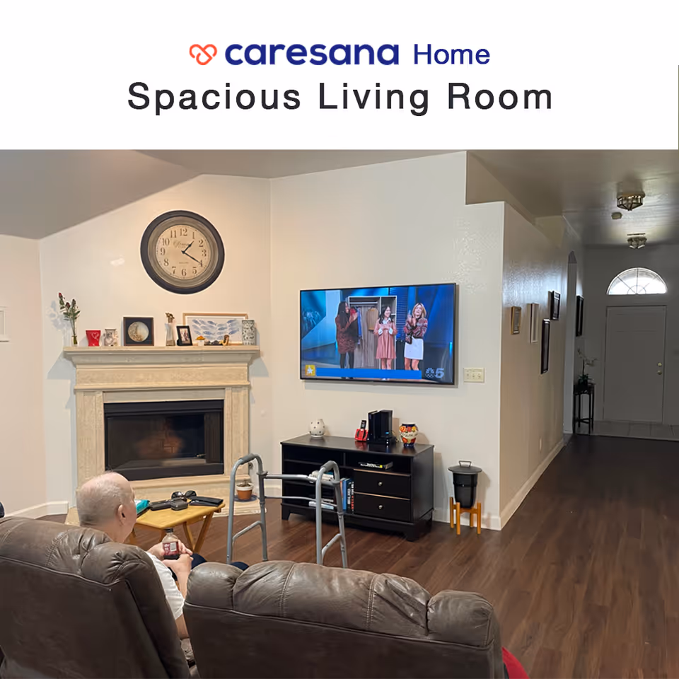 Living room with a fireplace, wall-mounted TV, recliners, a walker, and a seated person watching television.