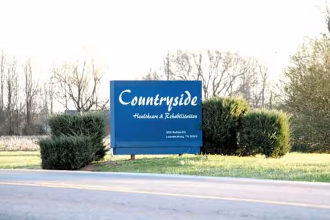 Blue Countryside Healthcare sign on a grassy verge beside a road.