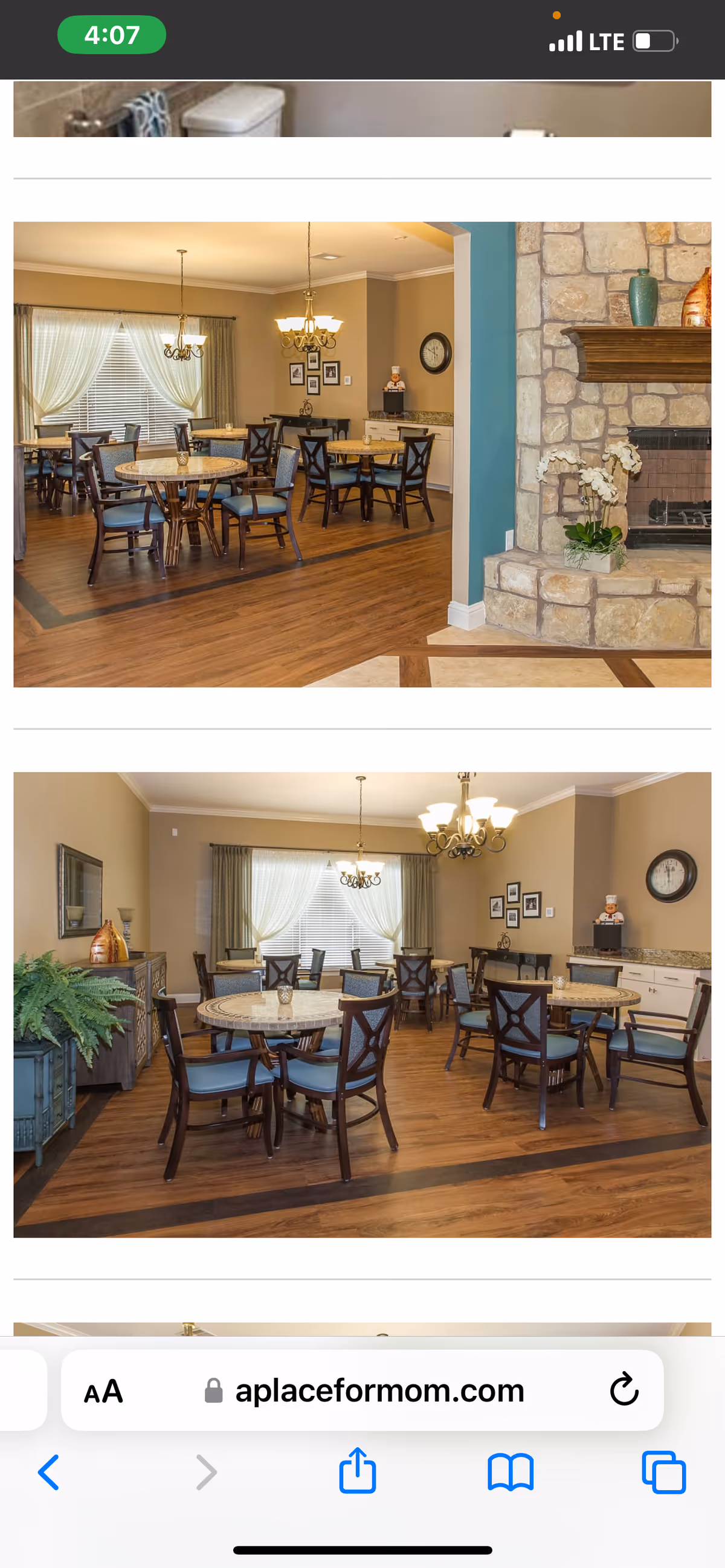 Two views of a dining room in an assisted living facility featuring round tables with chairs arranged around them. The room has wooden floors, beige walls, large windows with curtains, and chandeliers hanging from the ceiling. One view shows a stone fireplace with decorative items on the mantle and a plant beside it. The other view shows a sideboard with a plant and decorative items, along with a clock and framed pictures on the walls.