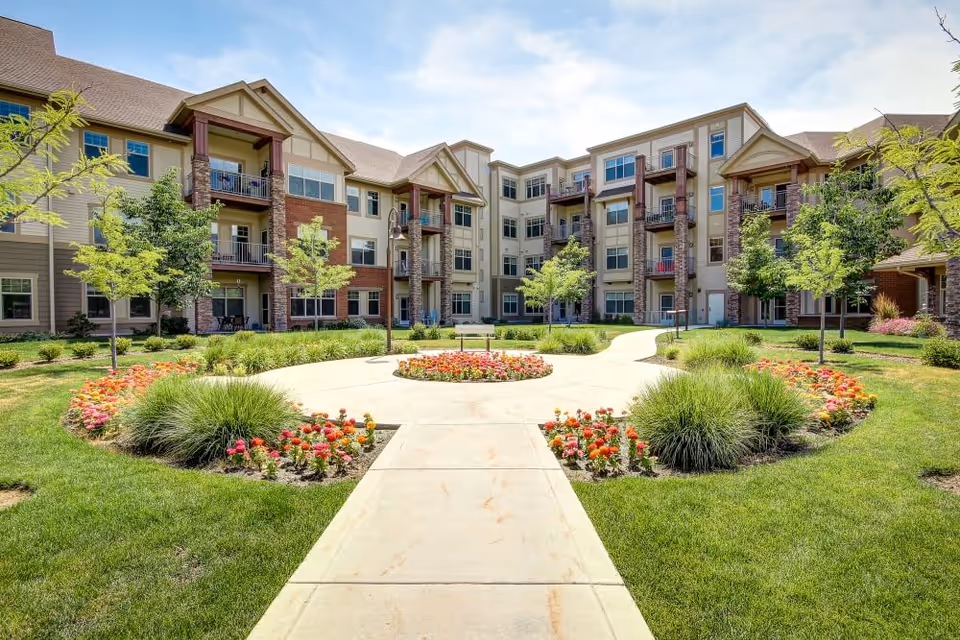 Landscaped central courtyard with a paved walkway, flower beds and a multi-story residential building with balconies.