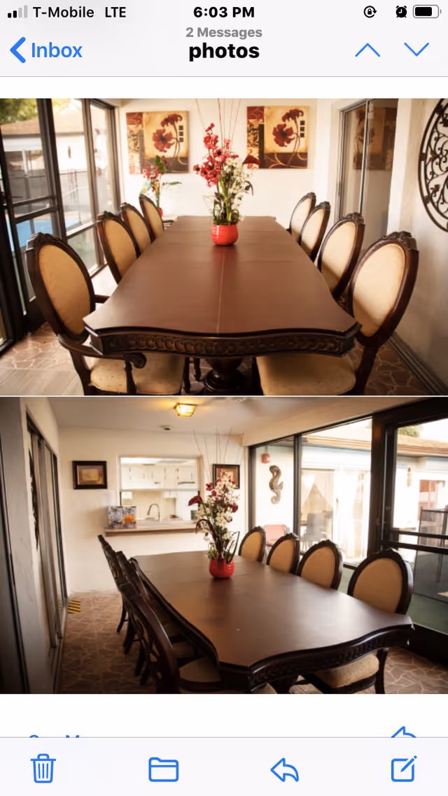 Two views of a dining room with a long wooden table surrounded by upholstered chairs. The table has a red vase with flowers in the center. The room has large windows and sliding glass doors letting in natural light. Wall decorations include floral paintings and a metal seahorse sculpture.