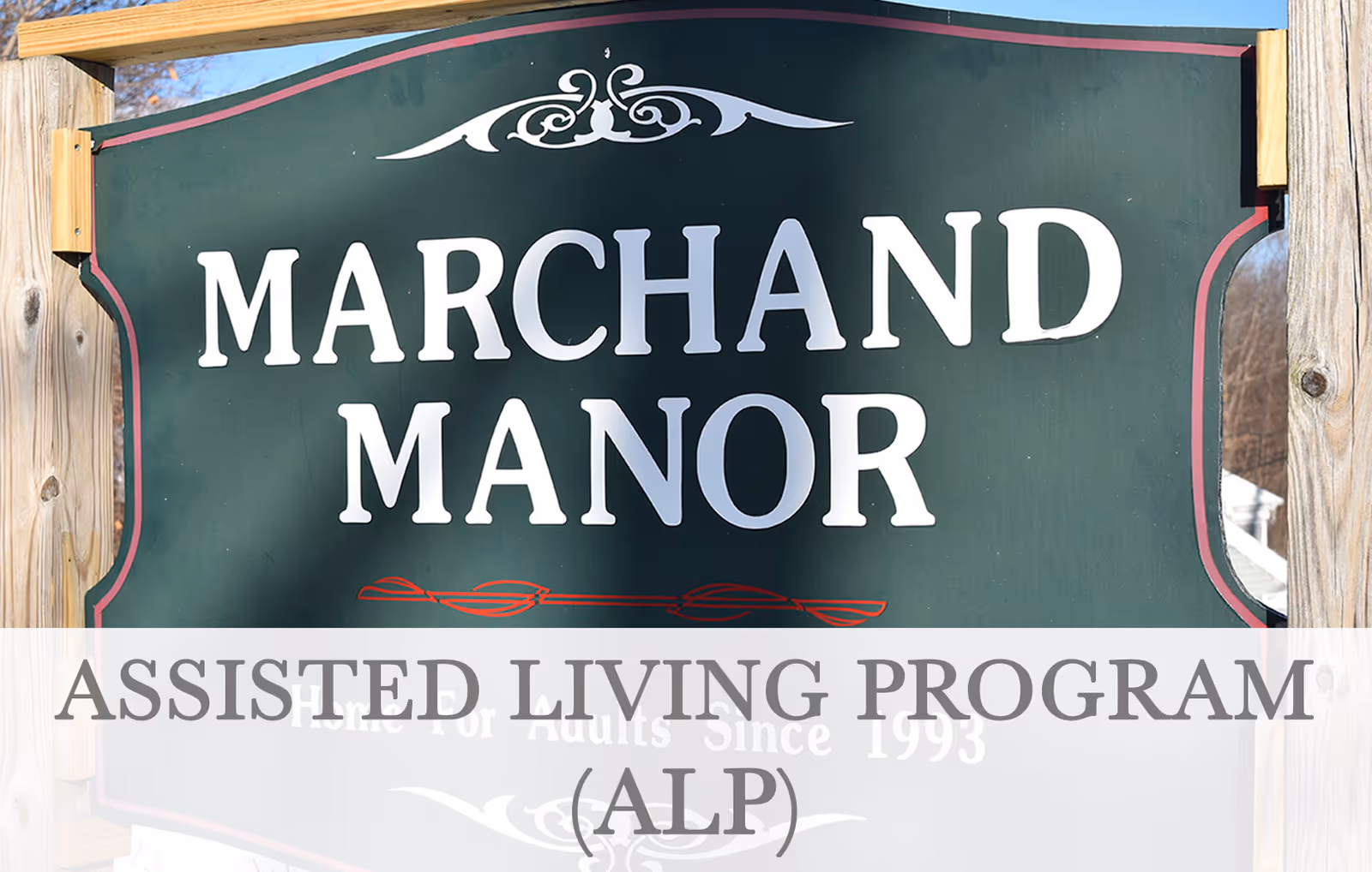 A green wooden sign with white text reading 'Marchand Manor' mounted on wooden posts outdoors, with a decorative design above the text and a red line below. The sign is partially covered by a translucent overlay with the text 'ASSISTED LIVING PROGRAM (ALP)'.