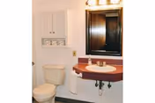 Small bathroom showing a toilet, wall-mounted sink with faucet and mirror, towel hanging, and a built-in wall cabinet.