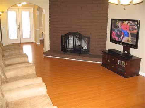 Living room with brick fireplace, wooden floor, TV, stairs on the left, arched doorway.