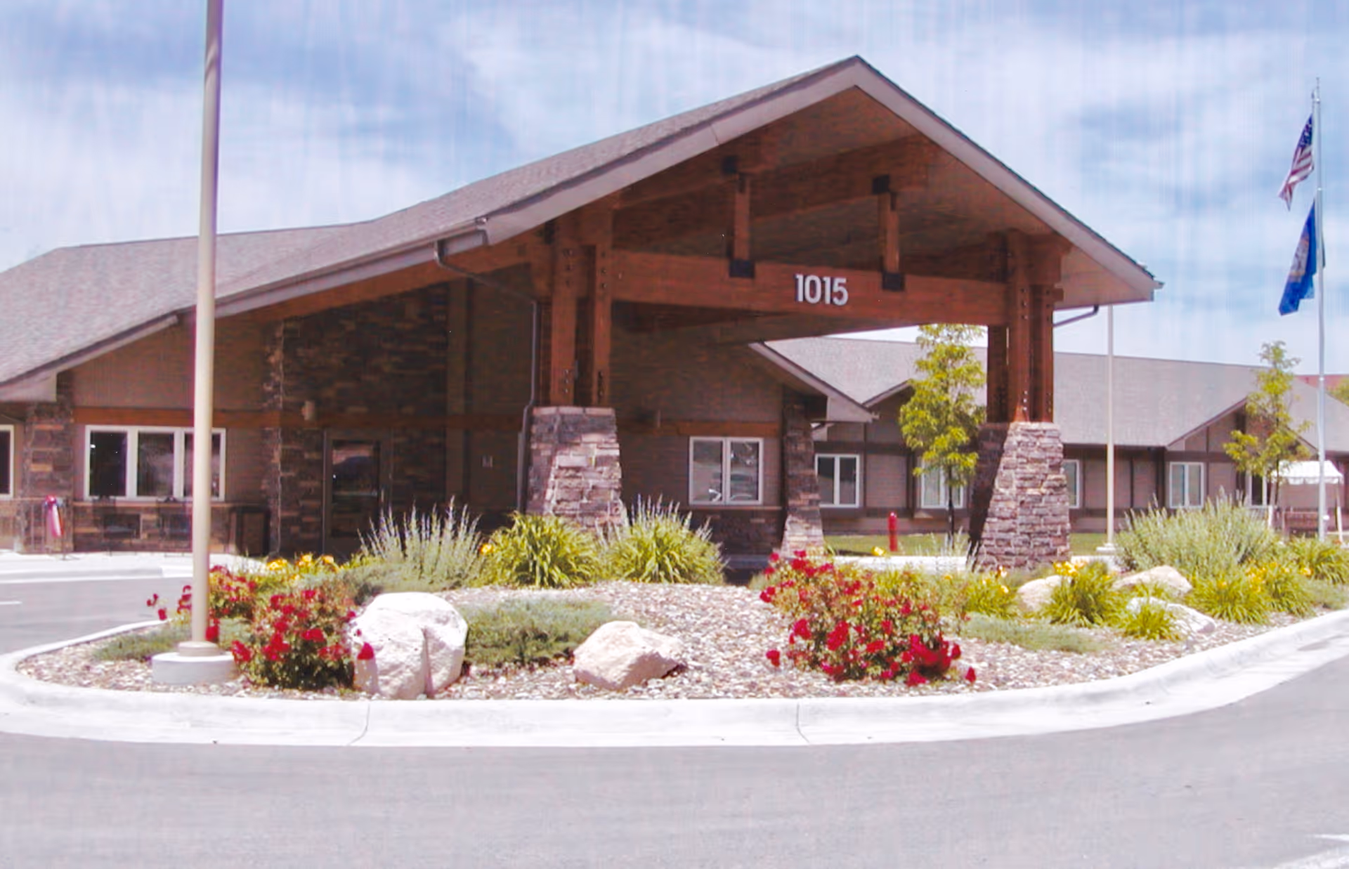 Front entrance of Clarkson Health Care with a covered porte-cochere marked "1015" and landscaped roundabout with flowers and rocks.