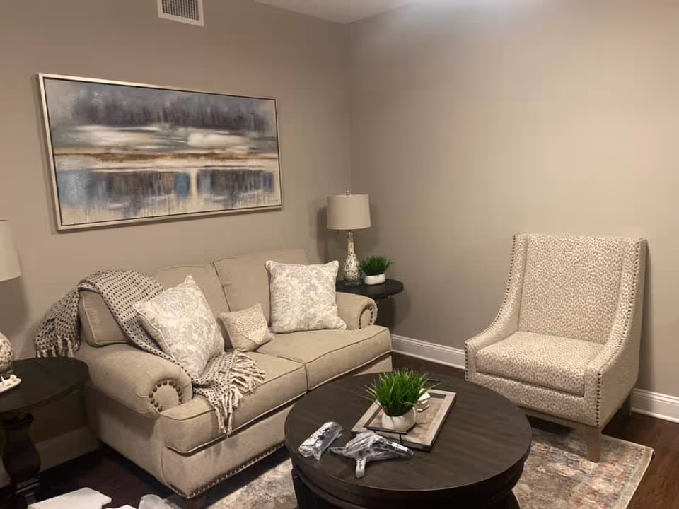 Neutral-toned living room with a beige sofa, patterned armchair, round coffee table and wall art.