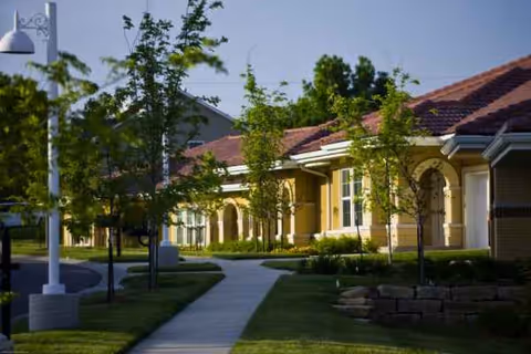 A senior living facility exterior with walkway and trees along the front.