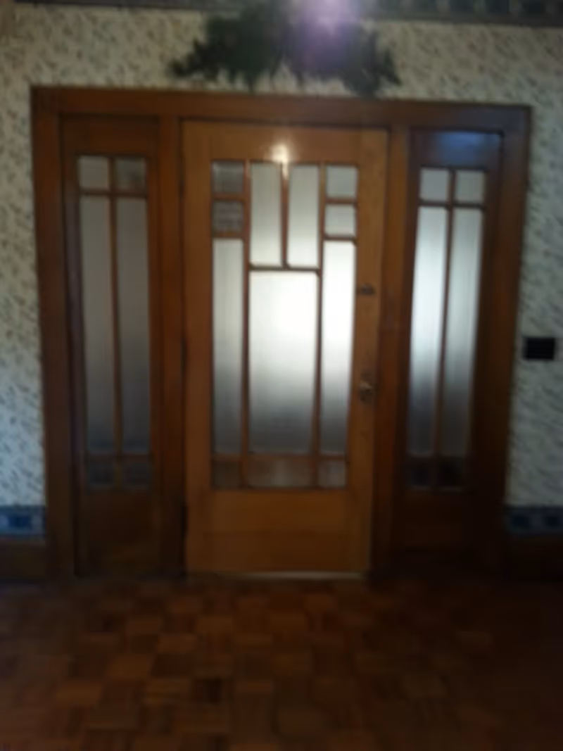 Wooden door with frosted glass panels in a patterned wallpapered room with wooden parquet flooring.