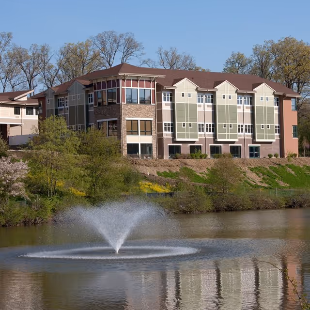 Multi-story senior living building along a pond with a central fountain.