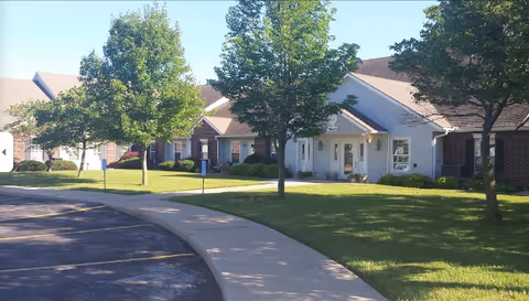 Exterior view of Elliott Place Senior Living with a curved sidewalk, lawn, and trees.
