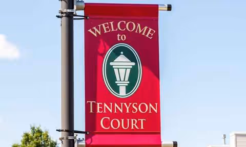 Red welcome banner reading Tennyson Court hangs from a pole against a blue sky.