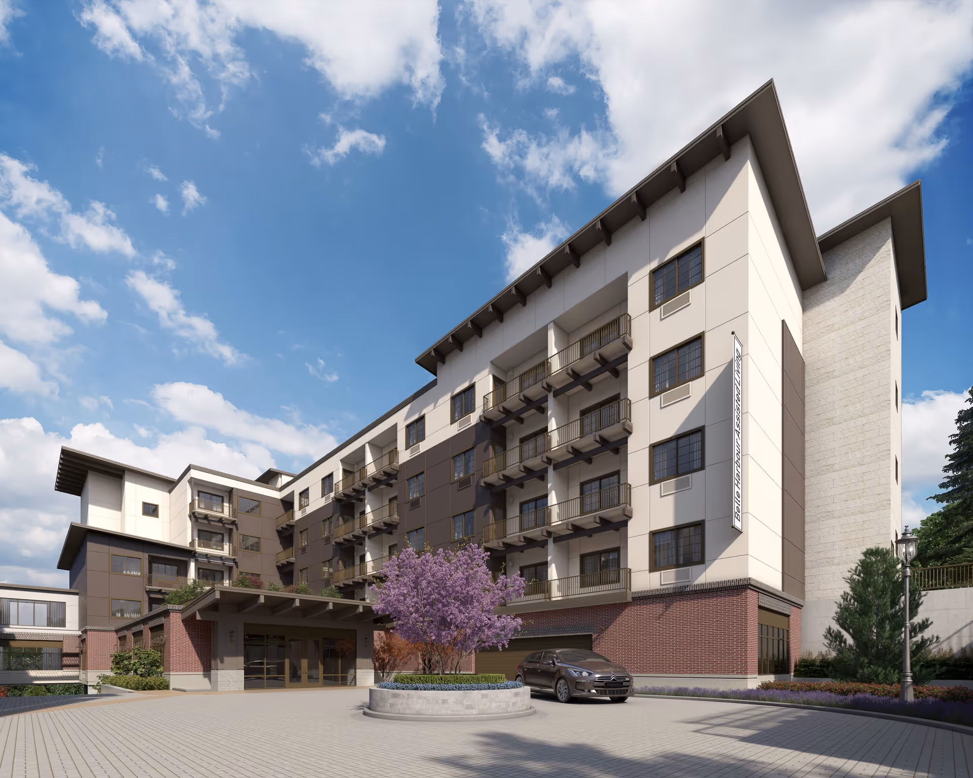 Exterior view of a multi-story assisted living community building with balconies, a covered entrance, a round planter with a blooming purple tree, a parked car, and a clear blue sky with some clouds.