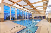 Indoor lap swimming pool with marked lanes, large floor-to-ceiling windows, and exposed wooden ceiling beams.