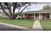 One-story brick retirement community building with a front walkway, manicured lawn, and a large tree.