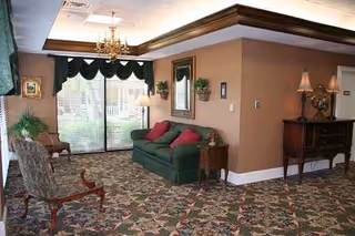 Cozy lounge in a senior facility with patterned carpet, green sofa, chairs, lamps, and chandelier.