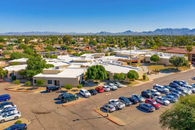 Aerial view of a single-story senior living complex with white roofs, a large parking lot, and mountains on the horizon.