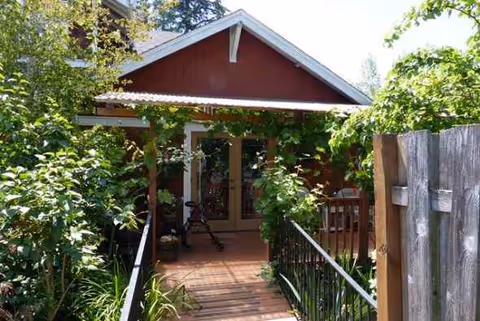 Red, cottage-style building entrance with ramp, railing, and lush greenery.