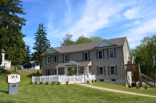Two-story beige building with white trim, front porch, and Ave Care sign on lawn.