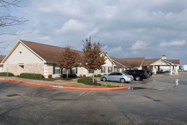 Exterior view of a single-story healthcare and rehabilitation center building with a beige and brick facade, several parked cars, and a covered entrance under a cloudy sky.